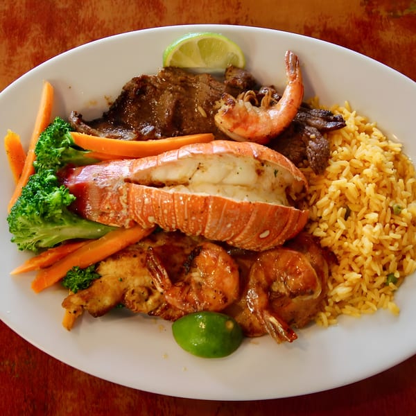 Surf and turf plate with lobster, shrimp, steak, yellow rice, and steamed vegetables.