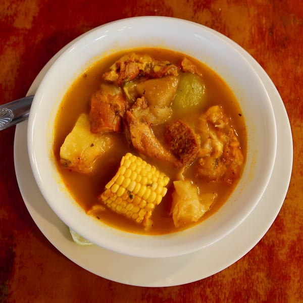 Hearty soup with corn, meat, and vegetables in a white bowl on a rustic red table.